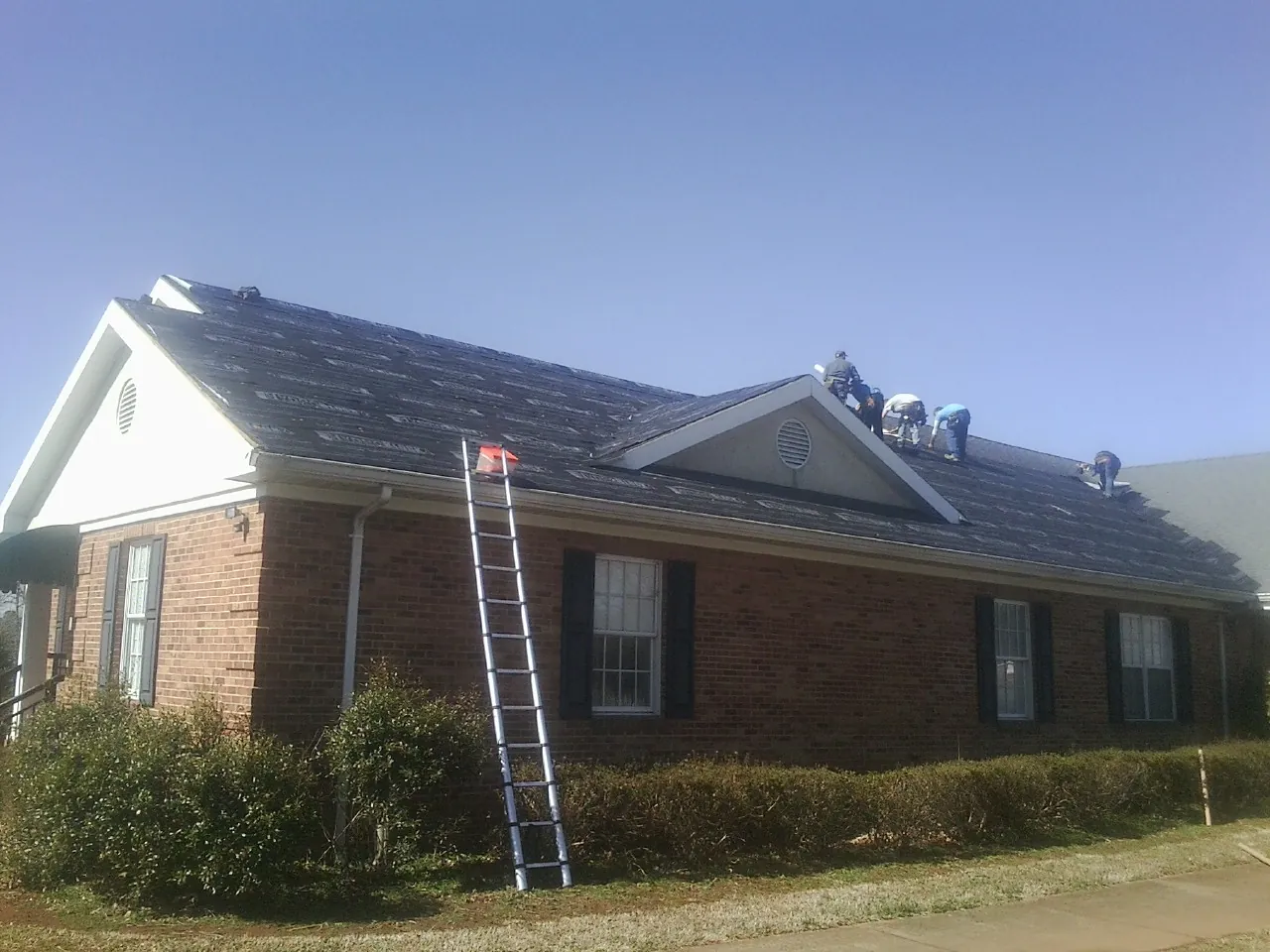 Crew tearing shingles off a brick ranch roof with a ladder set — Emergency Roof Repair work by our crew in Tremont