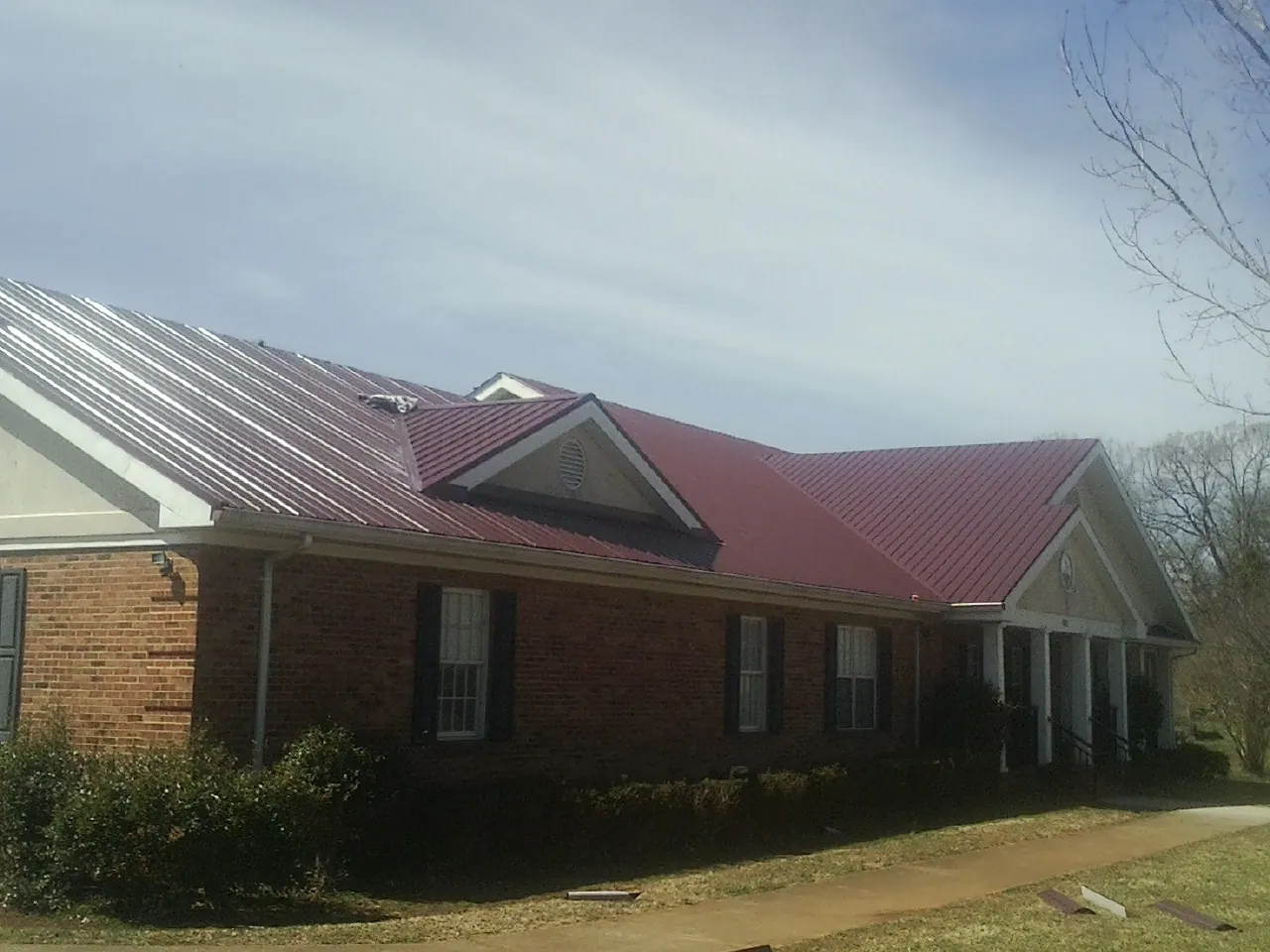 Red metal roof with gabled entries on a long brick building, from a Hail Damage Roof Repair job in Tremont