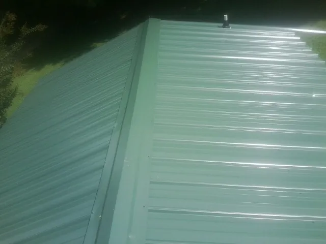 New green metal panels meeting at the ridge of a roof — Flat Roof Repair work by our crew in Tremont