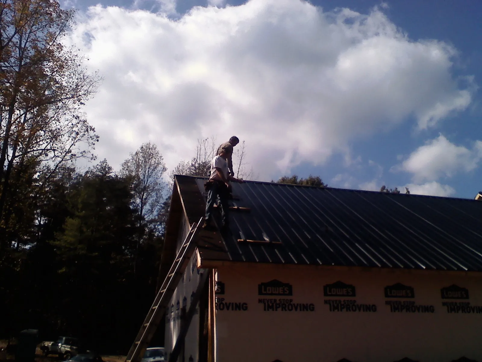 Roofer fastening dark metal panels high against a cloudy sky, from a Roof Inspection job in Tremont